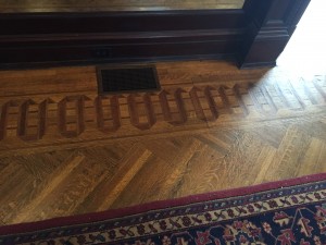 The perimeter of the living room floor is lined with intricate patterns using woods of different shades