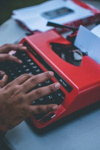 Hands typing on a red typewriter