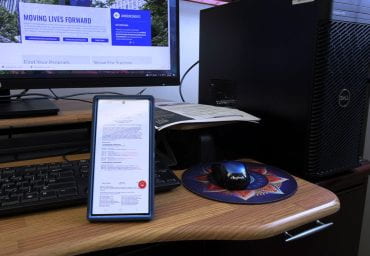A cellphone displays a PDF in front of a desktop monitor