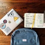 A laptop with stickers, a student planner, a backpack on a table