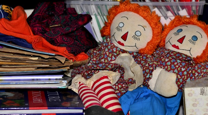 An image of old Raggedy Ann and Andy dolls, with other stored items such as books and old clothing.