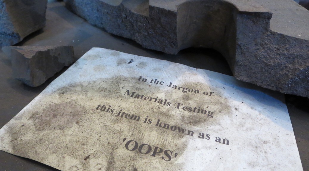Image of broken concrete form, with sign reading "In the jargon of materials testing this item is known as an 'oops'"